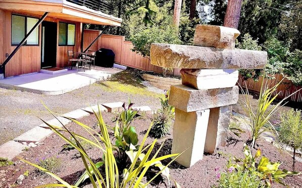 A modern building with a wooden exterior, a stone sculpture in the foreground, and a patio area with outdoor seating.
