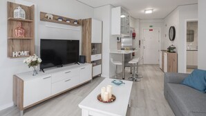Un salon moderne avec un téléviseur, des meubles blancs, une table basse avec des bougies et un canapé gris.