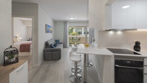 Une cuisine moderne dotée d’un îlot central, d’un coin repas avec des tabourets de bar et d’une vue sur un balcon aménagé avec du mobilier d’extérieur.