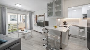 Une cuisine moderne avec des meubles blancs, un îlot central et un coin repas comprenant un canapé et une table.