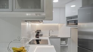 Une cuisine moderne avec des meubles blancs, un réfrigérateur en acier inoxydable, un four à micro-ondes encastré et un porte-bananes posé sur le plan de travail.