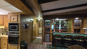 Una cocina con armarios de madera, microondas, horno y una barra con taburetes.