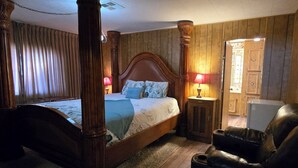 Una cama con dosel, un cabecero de madera, un sillón de cuero y una mesita de noche con una lámpara.