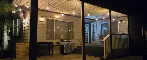 A covered outdoor area with a grill, string lights, and a view into a house.