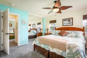 Un dormitorio con una cama, ventilador de techo, espejo y ventana.