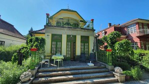 A building with a green and yellow facade, a balcony with a railing, and steps leading to the entrance. - Studio near the beach with internet (Siófok)