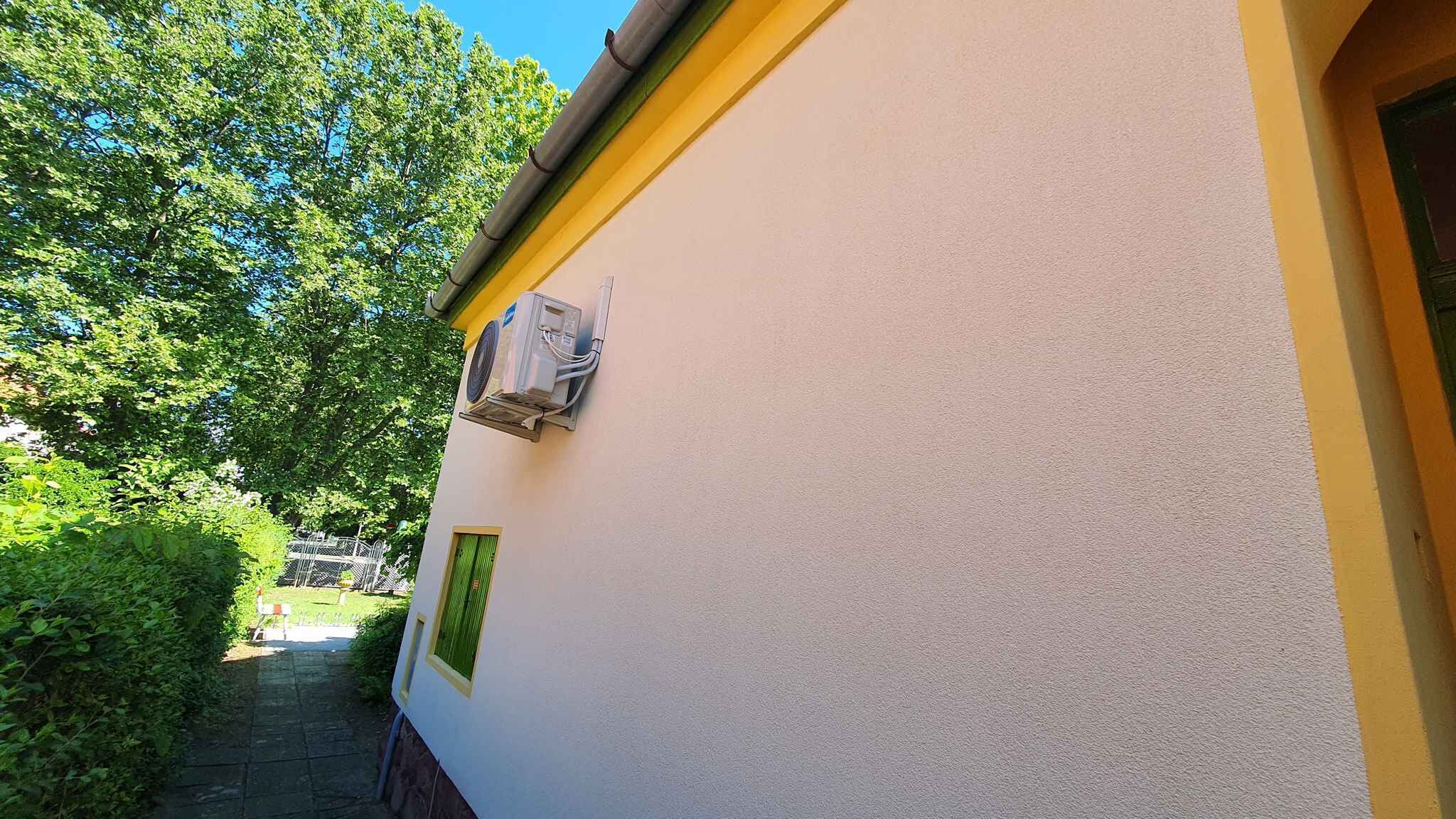 En bygning med hvide vægge og gul dekoration øverst. Der er et lille vindue med grøn ramme på siden.