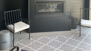 Un interior moderno con una chimenea empotrada de color negro, una zona de estar con una silla metálica y un reposapiés, y una alfombra estampada en el suelo.