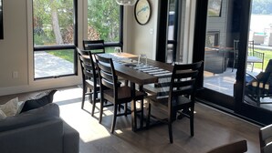 Un salón amplio con una mesa de comedor, sillas y un sofá. Grandes ventanas ofrecen vistas al exterior.