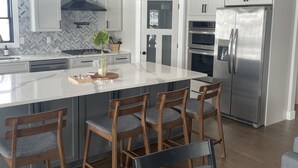 Una cocina moderna con una isla grande, sillas de madera, electrodomésticos de acero inoxidable e iluminación colgante.