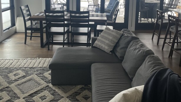 Amplia habitación con un gran ventanal con vistas a un cuerpo de agua, un comedor con mesa y sillas, y una zona de estar acogedora con sofá y alfombra estampada.