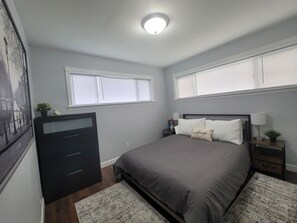 A bedroom with a bed, two bedside tables, a dresser, and a window with blinds. - Nice and cozy 1 bedroom apartment unit (Ypsilanti)