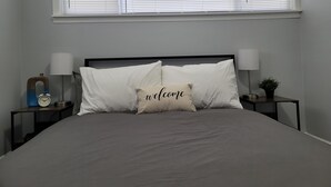 Un dormitorio con una cama, dos mesitas de noche, una lámpara de noche, una ventana con persianas y un reloj de pared.