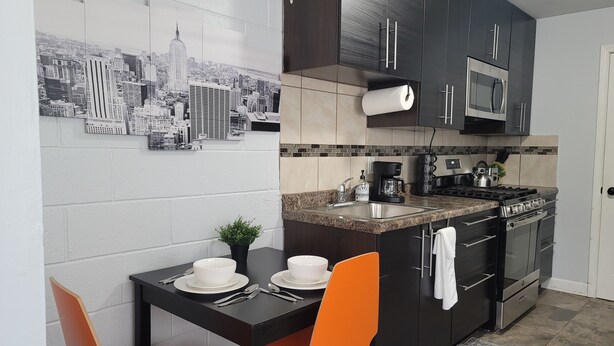 Una cocina moderna con gabinetes oscuros, encimera de granito, cafetera y un mural con vistas a la ciudad.
