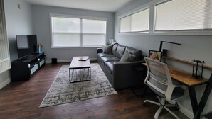 Una sala de estar moderna con un sofá de cuero negro, una mesa de centro de madera, un televisor y un escritorio con una silla.