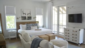 Een slaapkamer met een groot bed, een televisie, een dressoir en een raam met gordijnen.