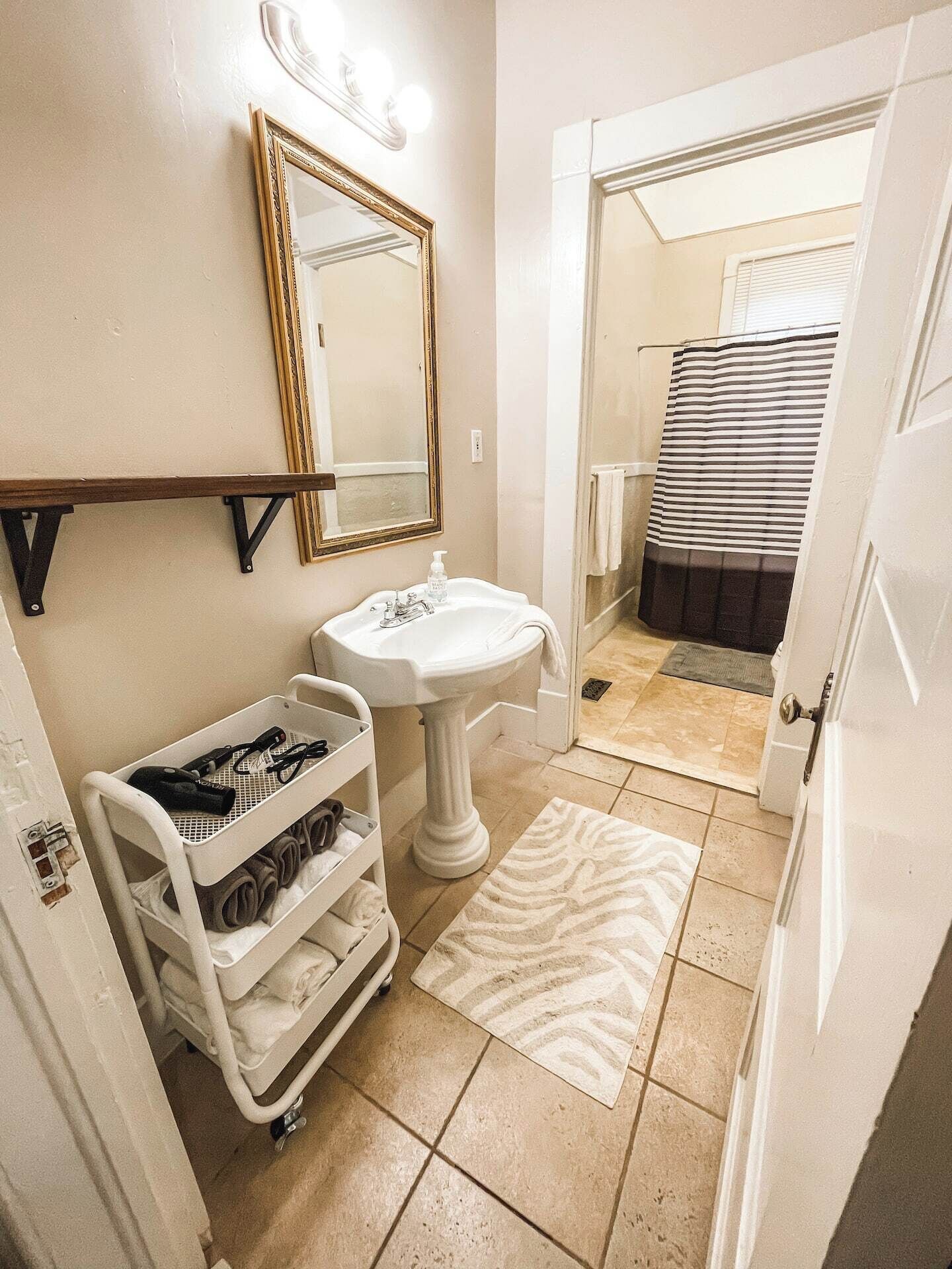 A bathroom with a pedestal sink, a mirror with lights, a towel rack, and a shower curtain.