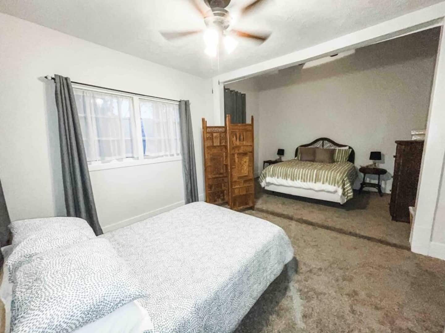 A bedroom with two beds, a wooden wardrobe, a ceiling fan, and a window with curtains.
