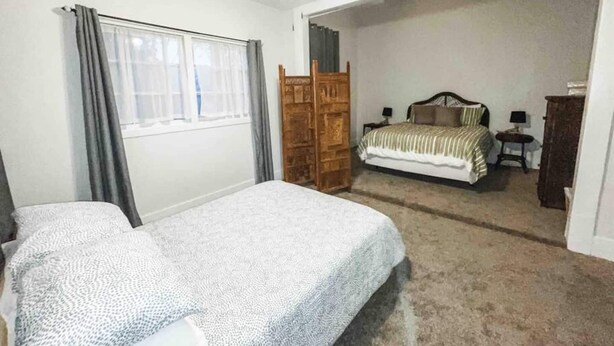 Un dormitorio con dos camas, un armario de madera, un ventilador de techo y una ventana con cortinas.