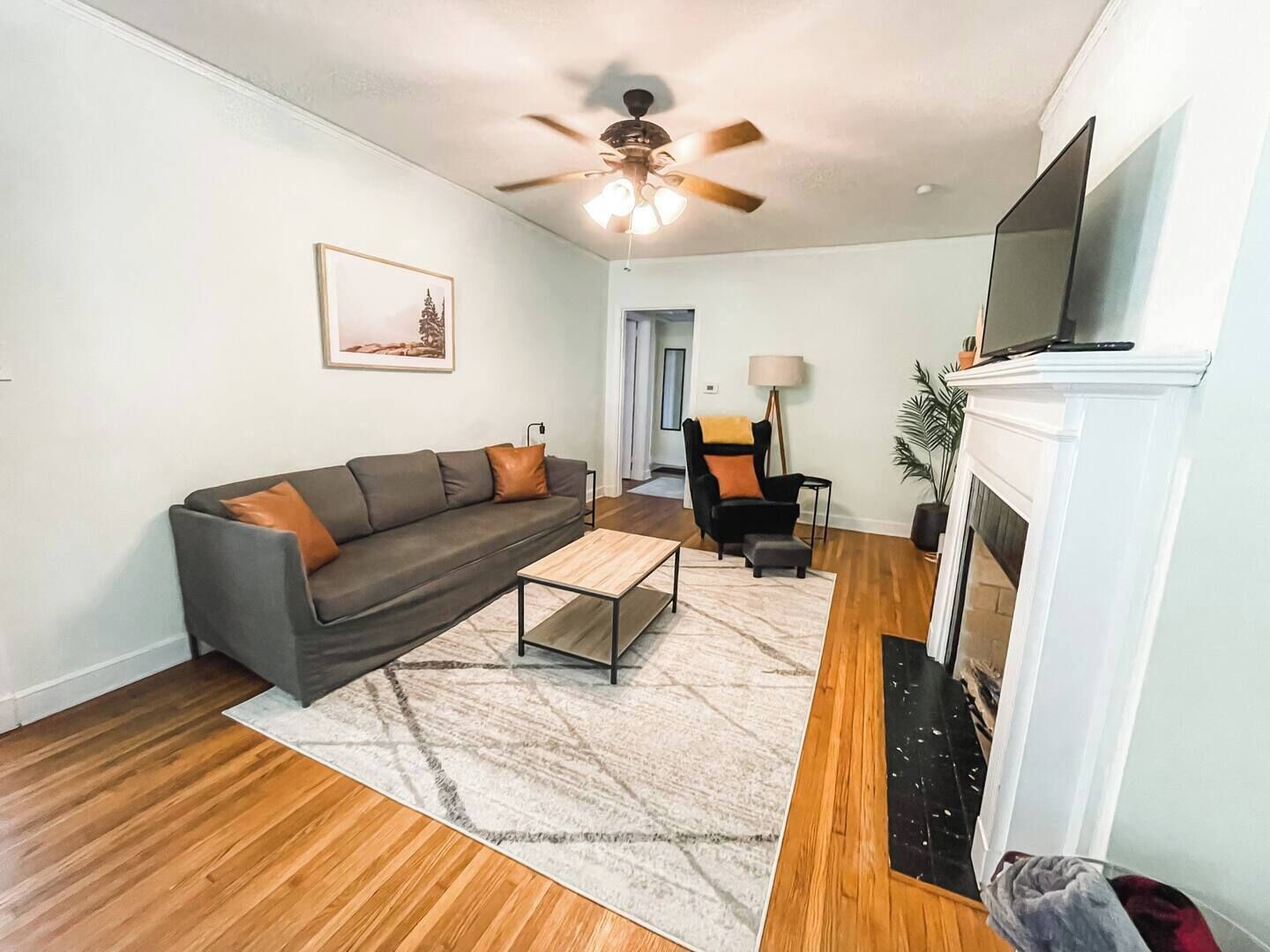 Una sala de estar con sofá, mesa de centro, chimenea, televisor y ventilador de techo.
