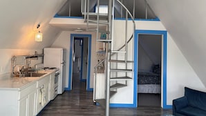 A compact apartment with a kitchen, a dining area, a staircase leading to an upper level, and a small living space.