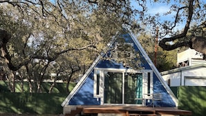 A small, triangular house with a wooden deck and a sliding glass door.