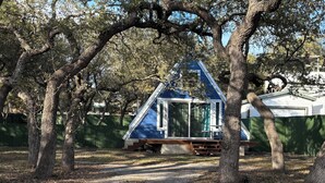 A small, blue, A-frame cabin surrounded by trees.