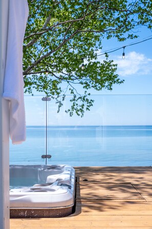 A hot tub with a view of the sea, a wooden deck, and a tree providing shade. - Fitzroy Lakehouse - Lake Ontario Waterfront with Hot Tub (Prince Edward)