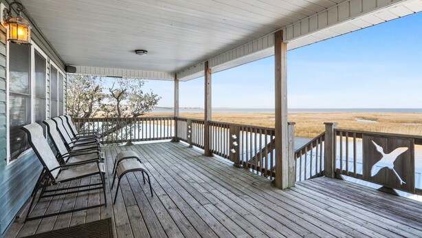 A covered porch with wooden railings and benches, overlooking a beach. - Black Dog Lodge & Fishing Charter- Waterfront! (New Orleans)