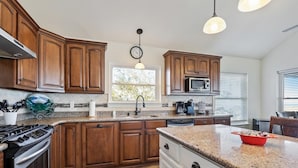A kitchen with wooden cabinets, granite countertops, a stove, a microwave, and a window with blinds. - Black Dog Lodge & Fishing Charter- Waterfront! (New Orleans)