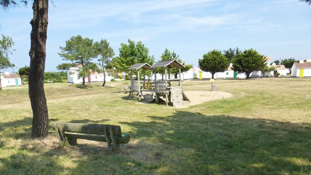 Un parc avec un banc en bois, des structures de jeux pour enfants et des maisons en arrière-plan.