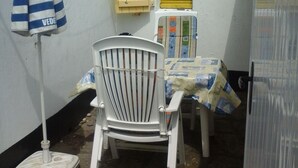 Un petit espace extérieur aménagé avec une chaise blanche, un parasol à rayures et une table recouverte d’une nappe colorée.