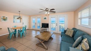A living room with a wooden coffee table, teal chairs, a teal sofa, a ceiling fan, and a TV.
