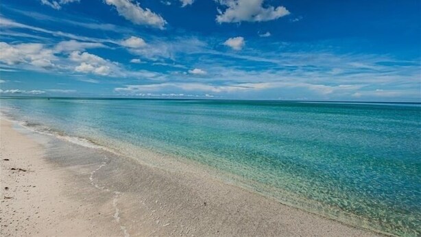A beach with clear turquoise water and a sandy shore under a blue sky with scattered clouds.