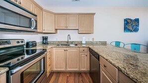 A kitchen with wooden cabinets, a granite countertop, a microwave, an oven, a sink, and a coffee maker.