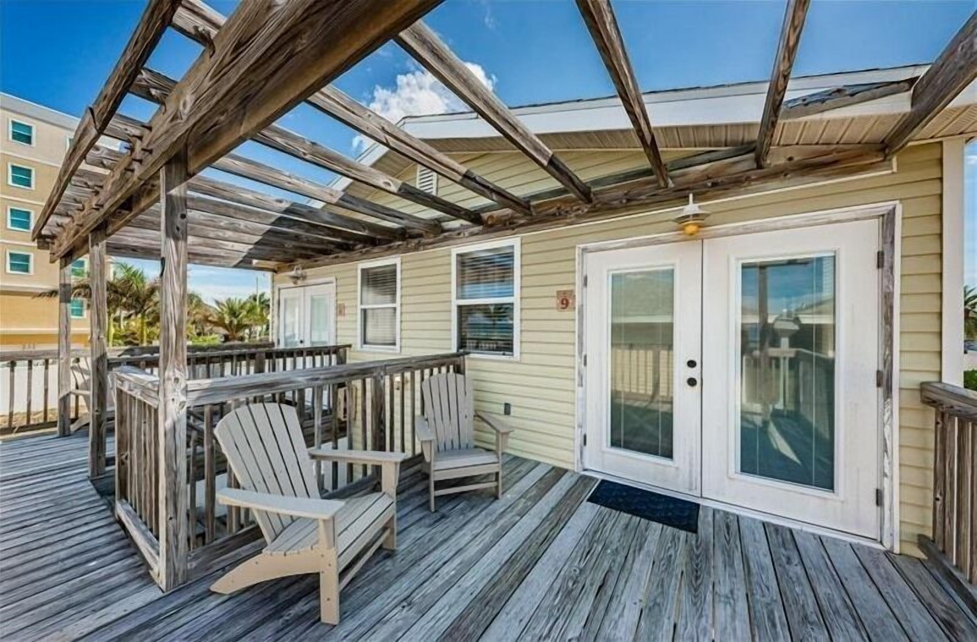 A covered outdoor deck with wooden chairs and a wooden railing.