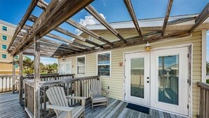 A covered outdoor deck with wooden chairs and a wooden railing.