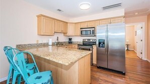A kitchen with wooden cabinets, a stainless steel refrigerator, a microwave, and a granite countertop.