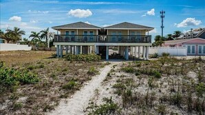 A two-story beachfront hotel with a balcony on the upper floor, a covered walkway, and a sandy beach in the foreground.