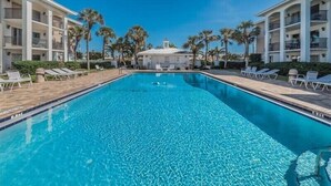 A rectangular swimming pool with clear blue water, surrounded by white buildings with balconies and palm trees. - Tortuga De Mar-Direct Gulf Front, Top Floor, Corner unit with Breathtaking Views & Magnificent Sunsets (Belleair Beach)