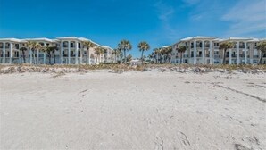 A beachfront hotel with a symmetrical facade, palm trees, and a clear blue sky. - Tortuga De Mar-Direct Gulf Front, Top Floor, Corner unit with Breathtaking Views & Magnificent Sunsets (Belleair Beach)