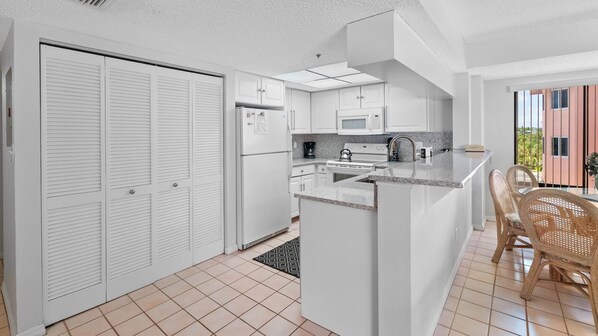 Una cocina moderna con armarios blancos, una isla central y una zona de comedor con sillas de mimbre.