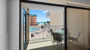 Un balcón con puerta de vidrio, una piscina y vista a un edificio y una playa.