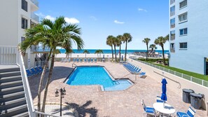 A pool area with a clear view of the ocean, surrounded by palm trees and lounge chairs.