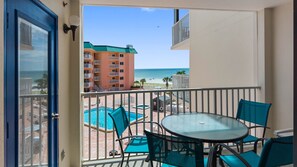 A balcony with a pool, chairs, and a view of the beach and ocean.