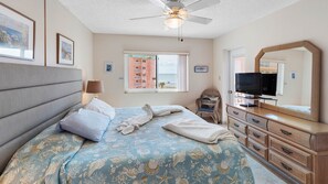 Habitación de hotel con cama, televisor, cómoda, silla y ventilador de techo.