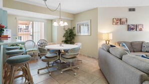 Un salon bien éclairé, avec une table ronde, des fauteuils confortables, un canapé et un coin repas avec des chaises en osier.
