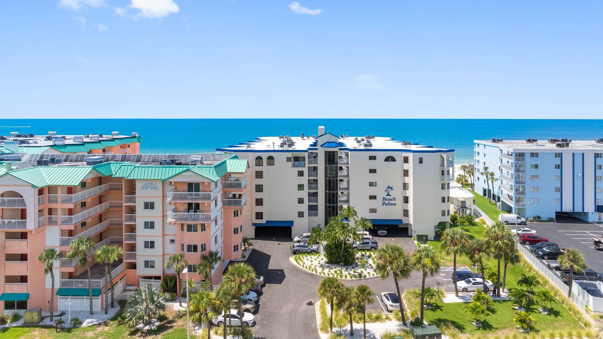 A beachfront hotel with multiple buildings, a parking area, and a clear view of the ocean.