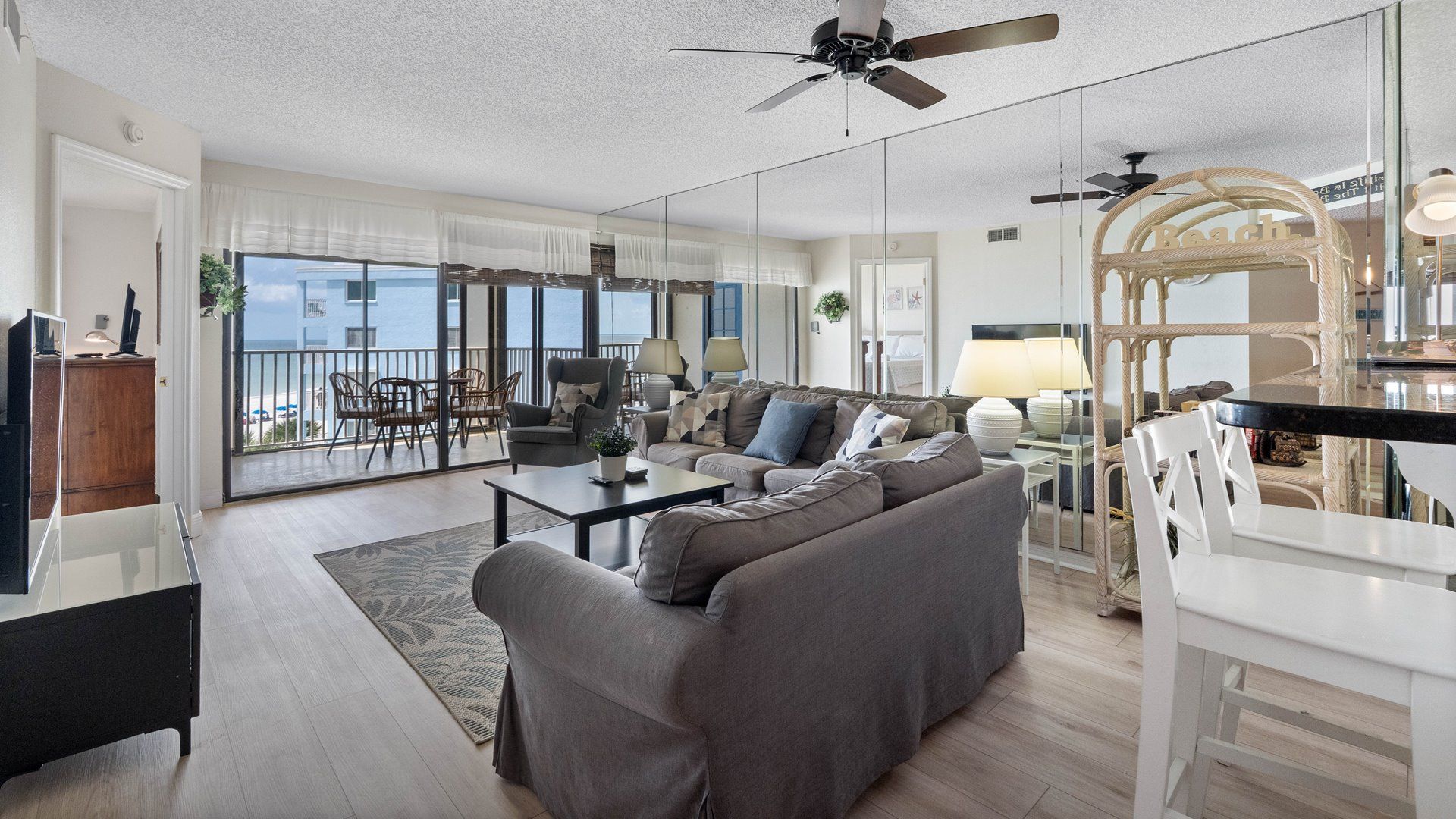 Un vaste espace de vie comprenant un canapé, une table basse et une table à manger. Un balcon offre une vue sur la mer.