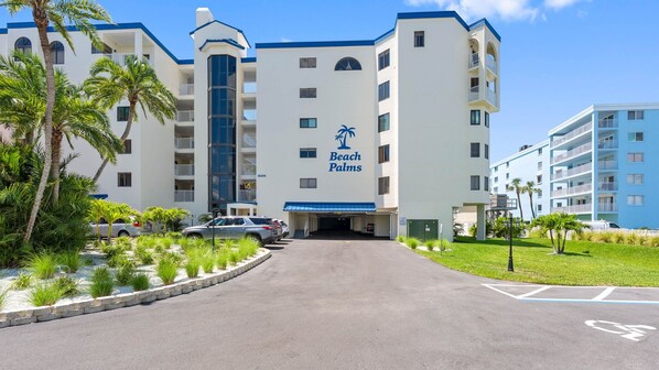 Un hôtel doté d’une entrée centrale, de nombreux balcons et d’une allée bordée de palmiers.